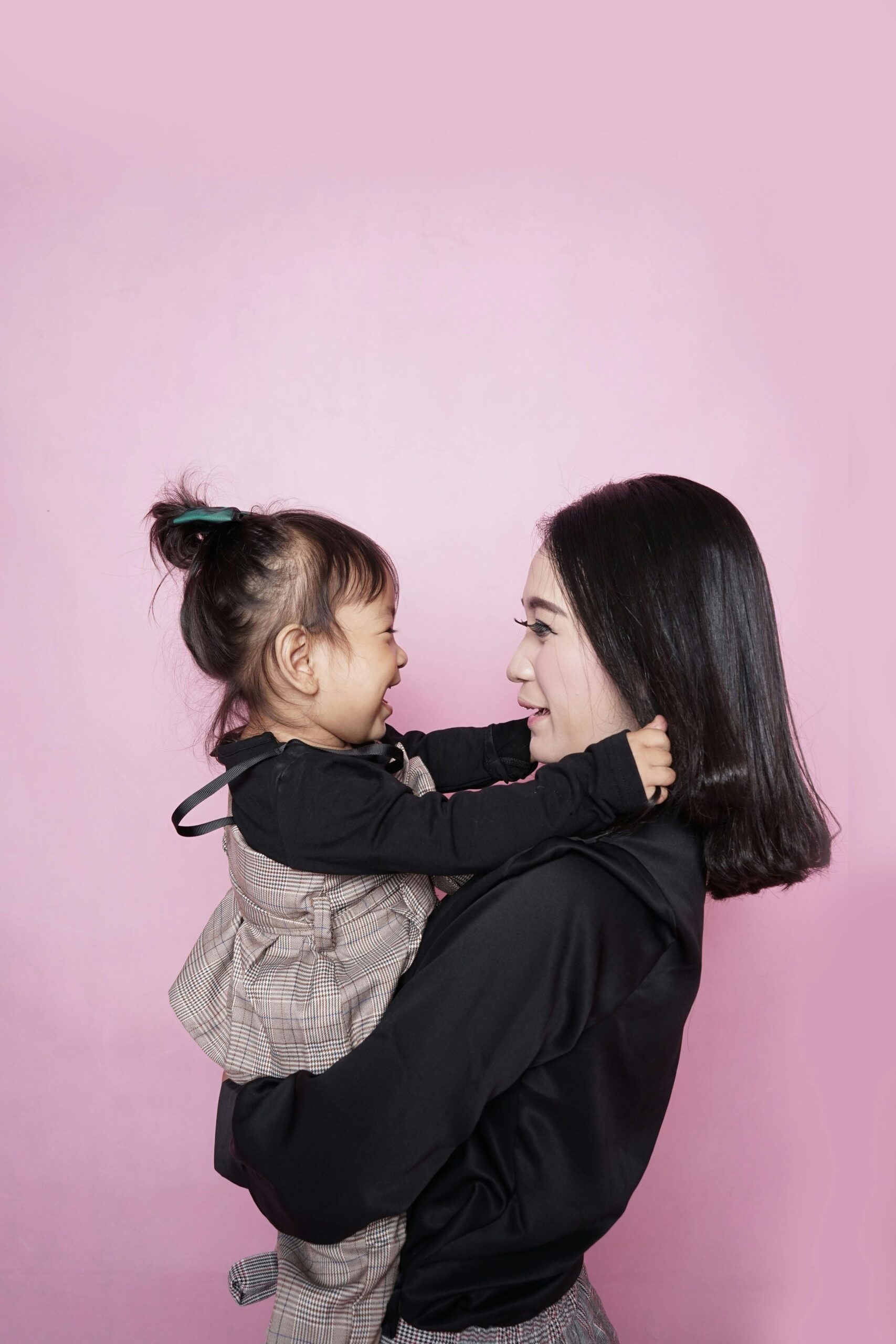 A happy mother holding her smiling daughter against a pink backdrop, showcasing love and togetherness.